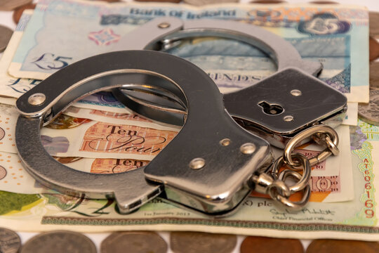 UK currency and handcuffs symbolizing fraud investigation and economic violations