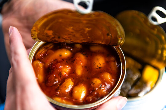 Giant baked cannellini beans in tomato sauce can storebought as vegan Greek food appetizer with herbs hand holding as snack