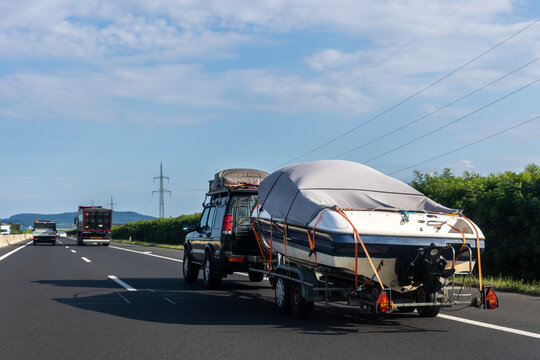 Big luxury cabin motorboat cruiser yacht trailer auto SUV carrier river lake highway road sunset summer light. Luxury rich fishing leisure recreation lifestyle. Service maintenance transportation