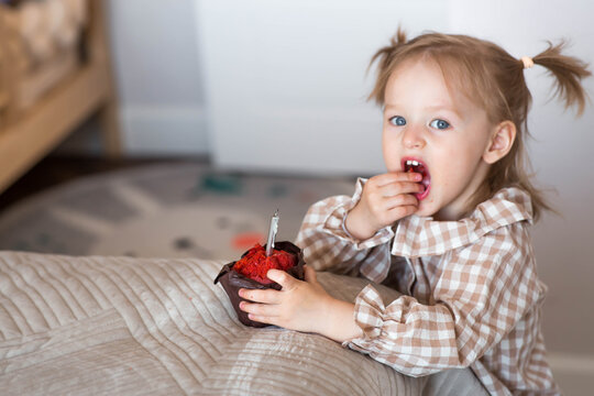 A little girl of 2 years old with a muffin or cupcake with a candle in a home environment. A festive morning. Happy Birthday.
