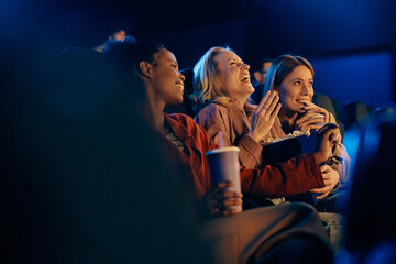 Happy woman laughing while watching comedy film with her friends at movie theater.