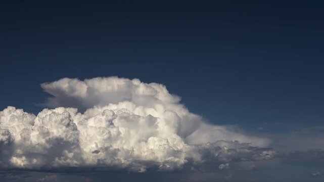 Timelapse of Massive Towering Cumulus Cloud With Boiling Texture on Deep Blue Sky, Isolated Without Ground, Dramatic Sunlit Relief and Large Copy Space