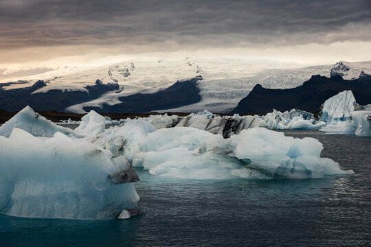 T&eacute;mpanos de hielo glaciar flotando en un lago en Islandia con vista a un atardecer nublado y monta&ntilde;as nevadas de fondo
