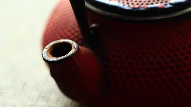 A close-up view of a bright red teapot on a table, ready to serve hot tea