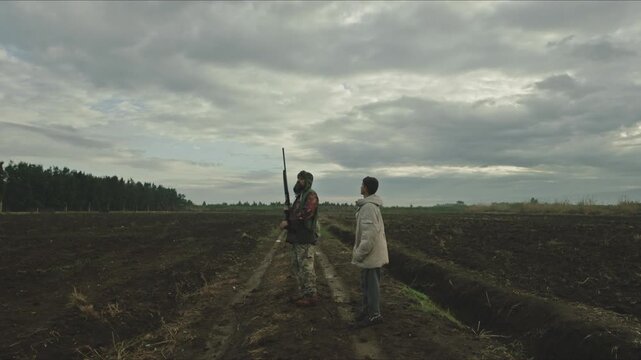 Experienced hunter teaching his son how to hunt in a rural field under a cloudy sky