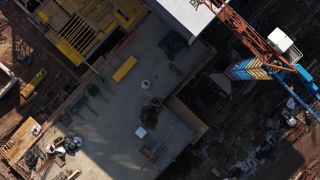 Drone shot of a multi-level concrete building frame with scaffolding, stairs, and organized construction materials on-site, highlighting structural development and engineering progress.