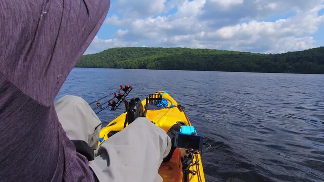 Man pedaling and paddling on PDL kayak for fishing at serene lake. Fishing sport angler using UV protective head hood or balaclava neck gaiter as sun mask. Fishing summer vacation.