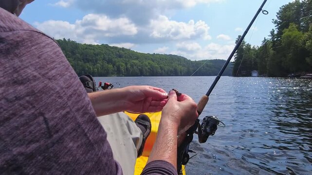 Angler put night crawler bait on fishing hook, drop shot fishing technique. Kayak sport fishing. Angler enjoys kayak fishing at scenic coastline. Peaceful water setting at lake Simcoe, Ontario, Canada