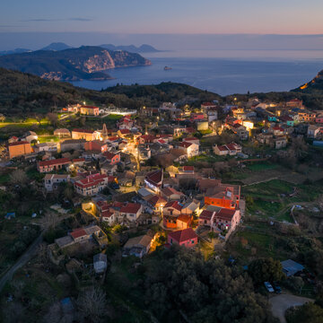 Aerial panoramic view of Krini village illuminated at twilight with Angelokastro fortress and dramatic Ionian Sea coastline in background on Corfu island Greece