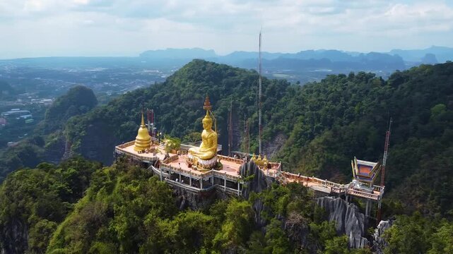 Drone orbit around a golden Buddha statue at Wat Tham Suea temple in Krabi Thailand.