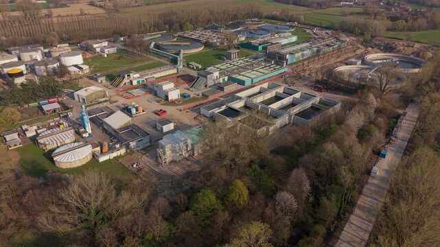 Industrial Water Treatment Facility: Aerial view of a large water treatment plant with multiple processing units, tanks, and pipelines under a clear sky.