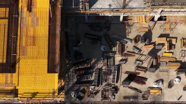 Top-down drone shot of a construction site showing yellow formwork panels, steel reinforcement bars, and organized materials on a concrete slab in active building development.