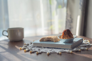 Cozy morning still life with a cup of coffee and small dessert on a wooden table near a sunny...