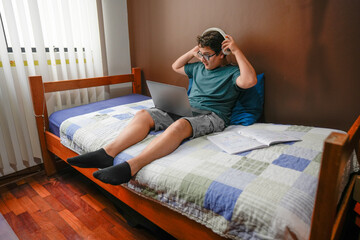 Obraz premium Teenager studying at home using laptop and headphones