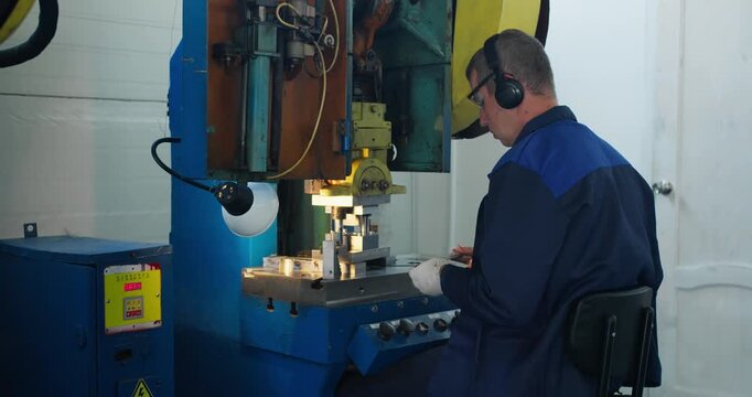 Blue collar operator working at industrial press machine with metal parts. Factory process and metalworking production