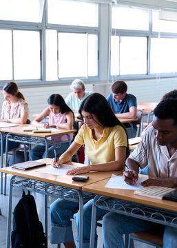 Vertical. Diverse students write an exam at their desks, showing focus, education, and academic assessment.