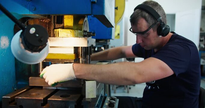 Blue collar factory worker handling metal components at press machine. Manufacturing workflow and industrial workshop activity