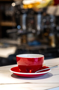 Bright red cup sits on a white saucer on a cafe counter during a busy morning