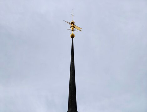 Bright steeple amid storm clouds. Lavish weather vane atop church pierces gloomy overcast atmosphere
