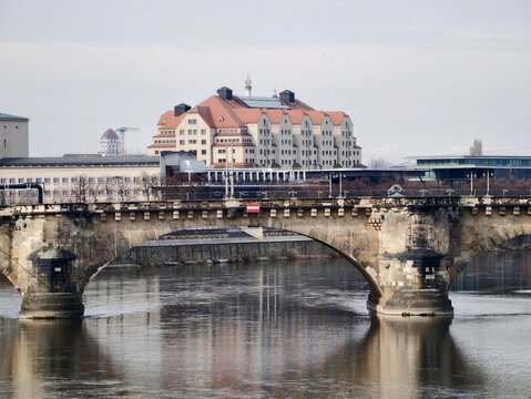 Timeless stone bridge stretching across serene water with nearby city skyline and subtle figures