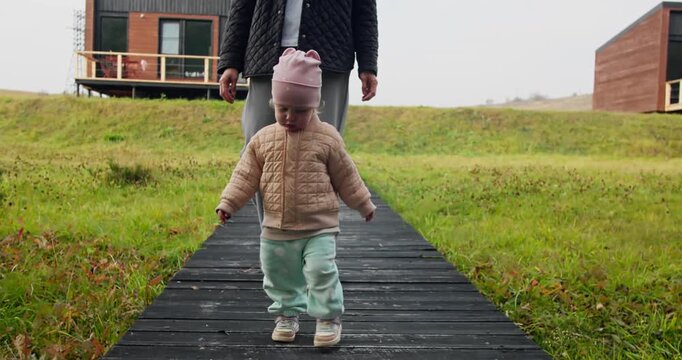 Young child practicing walking with mother nearby, first steps and early childhood development in calm