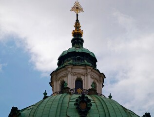 Exquisite baroque dome adorned with gilded finial and aged copper patina under cloudy skies © Vladimir