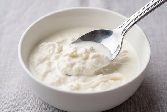 Silver spoon gently scooping creamy italian stracciatella cheese from white bowl