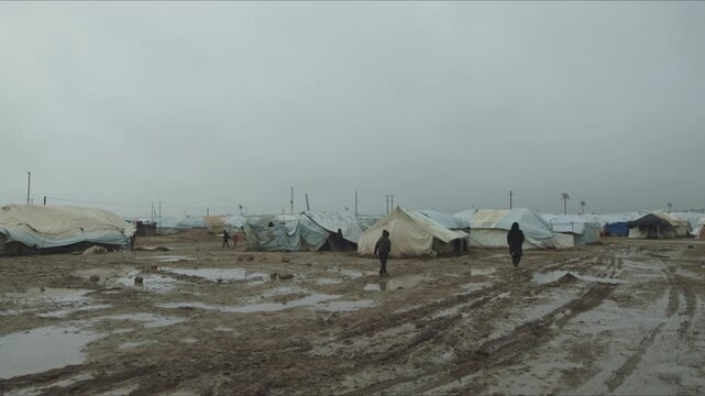 People walking through a muddy and squalid refugee camp after the rain in a Middle Eastern country