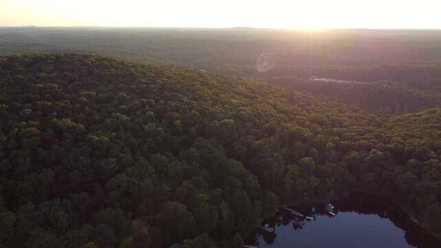 Buckskin Lake into the sun with lens flare on a summer afternoon. Aerial over lakeside cottages next to expansive crown land wilderness in Tory Hill, Halliburton Highlands East, Ontario, Canada.