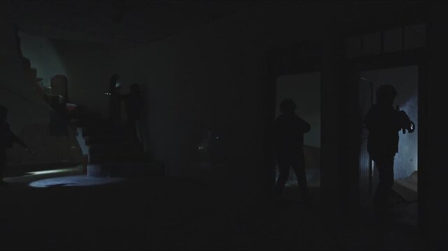 Armed special forces team with flashlights searching a dark, abandoned building during a raid