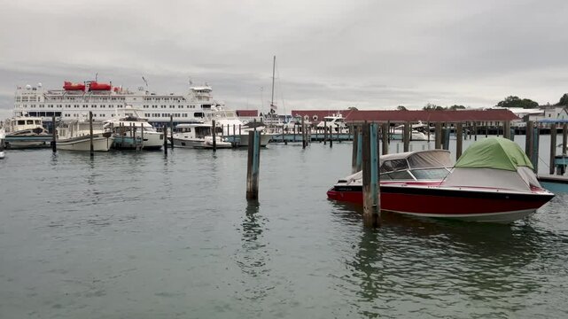 Peaceful scene at Mackinac Island State Harbor, MI, featuring sailboats and motorboats docked and bobbing. Overcast sky creates soft, even lighting over the Lake Huron shoreline.