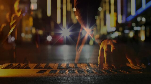 Male musician hands playing keyboard for street set, headlights appearing and casting light streaks