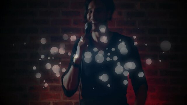 Male singer shifting mic upward revealing torso singing engaging music fans as light orbs drifting