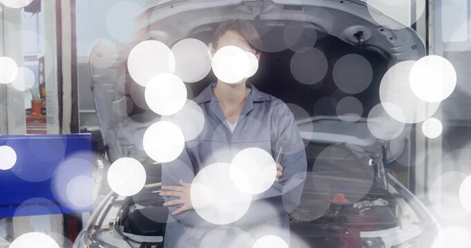 Female mechanic standing at open hood in auto shop, overlay starting, bokeh showing engine for demo