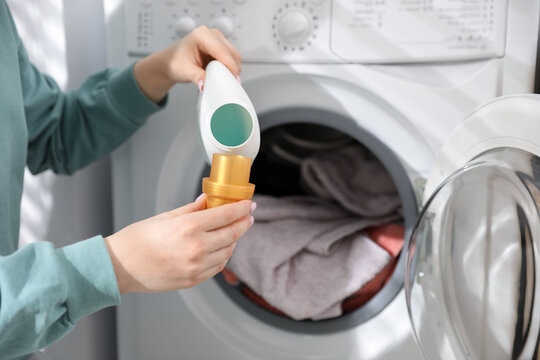 Woman adding detergent into washing machine at home, closeup