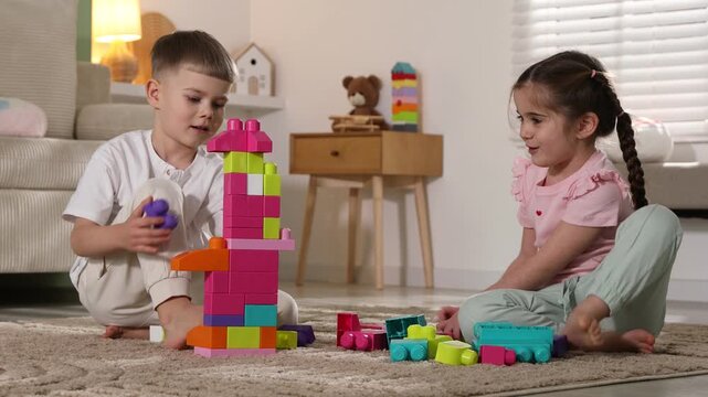 Smiling little friends playing with building blocks on floor at home