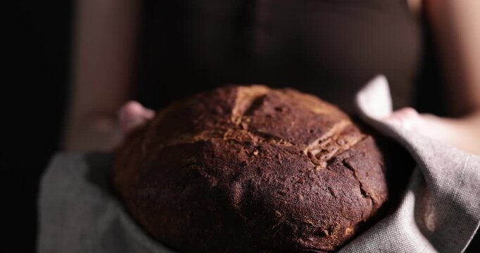 Woman holding loaf of rye bread on black background, closeup