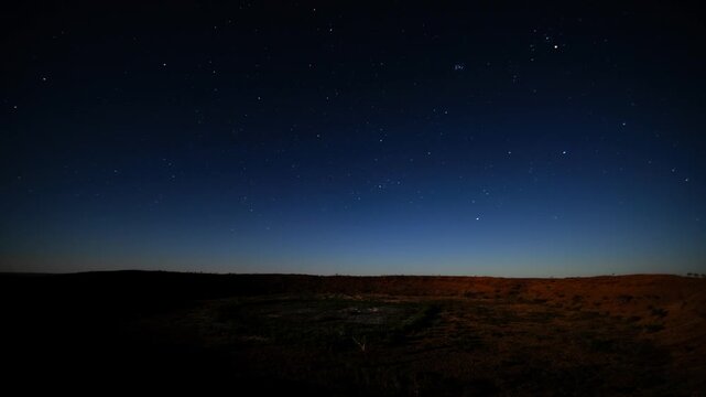 The starry sky moving and gradually fading over a vast, arid landscape as twilight disappears