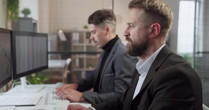 Businessman analyst at computer in office accounting report. Two colleagues analyze reports on dual screens, showing teamwork and analytics for budgeting, balance. Finance team plans for wise plans.