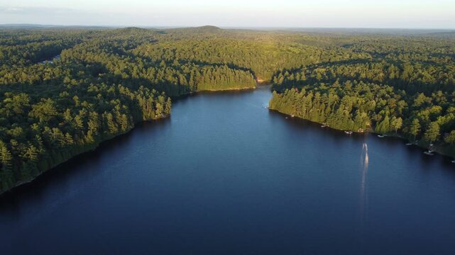 Flying over Buckskin Lake on a late summer afternoon shortly before sunset. Aerial above lakeside cottages along side wilderness of crown land in Tory Hill, Halliburton Highlands East, Ontario.