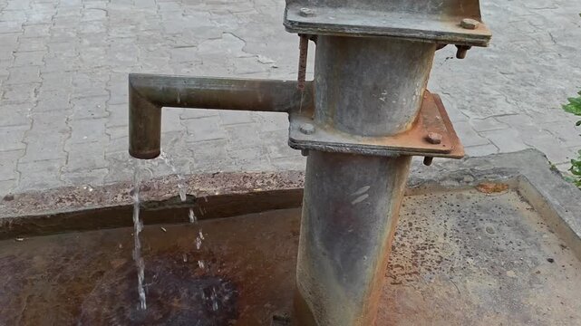 Fresh water flowing from a traditional rusty iron hand pump
