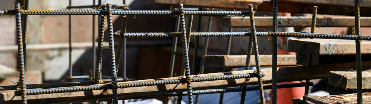 Construction job site, supply of iron rebar formed into square mesh panels and propped up, ready for installation as support in concrete pour, industry background
