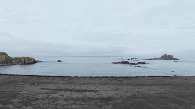 moves forward and rises over the black volcanic sands of Elephant Point, revealing the rugged basaltic coastline, distant sea stacks, and the cold waters of the Bransfield Strait, Antarctica