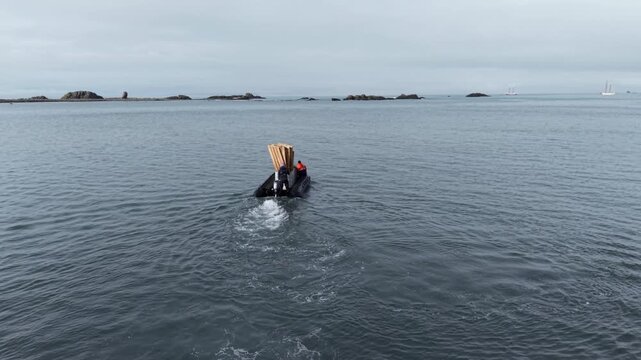High-angle aerial of an inflatable Zodiac boat carrying wooden pallets and equipment from Fedor Konyukhov's dismantled solo station at Elephant Point back to the expedition ship