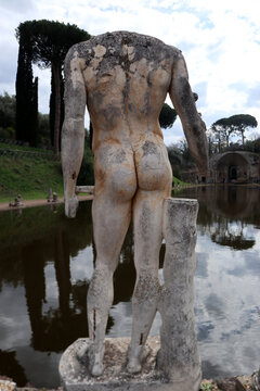 Veduta posteriore di una statua maschile acefala in marmo situata sul bordo del Canopo di Villa Adriana a Tivoli con riflessi degli alberi sullo specchio d'acqua