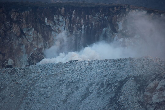 A massive dust cloud erupts from a controlled explosion at a marble quarry in Buner, Pakistan, showing the raw power of industrial mining against a rugged mountain cliff.