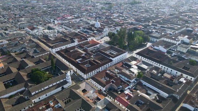 Aerial shot over Popayan's white colonial blocks showing red tile roofs, a tree-lined central plaza and a church dome.