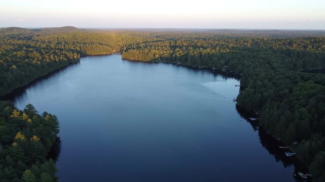 Aerial over Buckskin Lake during golden hour on a summer afternoon before sunset with lakeside cottages by expansive crown land wilderness in Tory Hill, Halliburton Highlands East, Ontario, Canada.