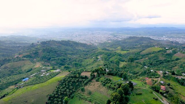 Drone panorama of rolling green farmland and scattered houses with Popay&aacute;n city visible on the hazy horizon beneath a cloudy, overcast sky.