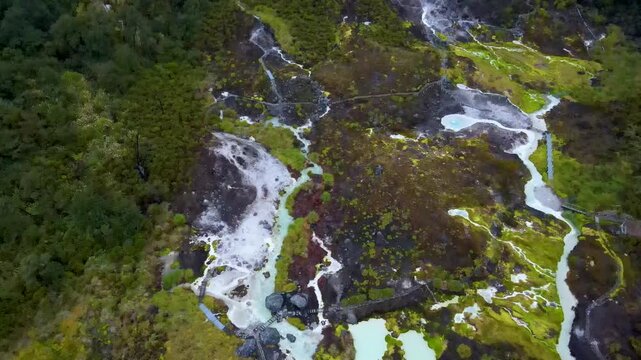 Drone view of Purace hot springs with pale turquoise pools and white mineral terraces winding through mossy highland and wooden boardwalks.
